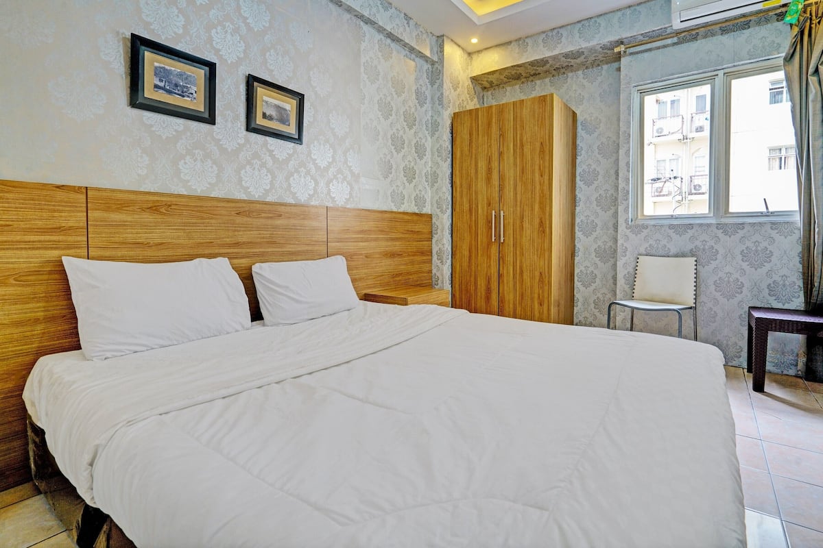 Een net opgemaakt bed in een hotelkamer met een houten hoofdeinde, een grote garderobe en een stoel.