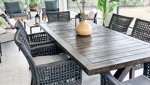 A dining area with a large wooden table surrounded by wicker chairs, a ceiling fan, and large windows offering a view of the outdoors. - A charming canal front home...close to the beach, and perfect for boat lovers! (Bonita Springs)