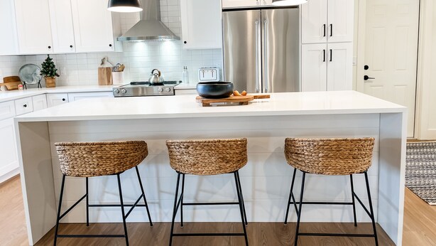 A modern kitchen with white cabinets, a stainless steel refrigerator, a gas stove, and three woven bar stools. - A charming canal front home...close to the beach, and perfect for boat lovers! (Bonita Springs)