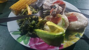 Ein Teller mit einer Auswahl an Speisen, darunter Mais, Fleisch, Avocado und Grünzeug.