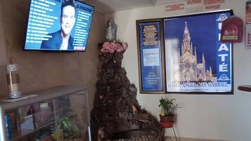 A hotel lobby with a large TV screen displaying a program, a decorative rock wall, a potted plant, and a framed picture of a cathedral.