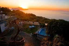 Un resort con piscina, sillas de descanso y vista al atardecer sobre el océano.