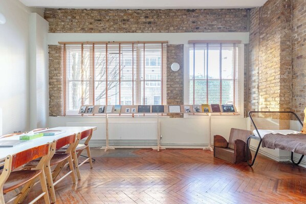 A room with a brick wall, wooden floor, a table with chairs, and a window with blinds.