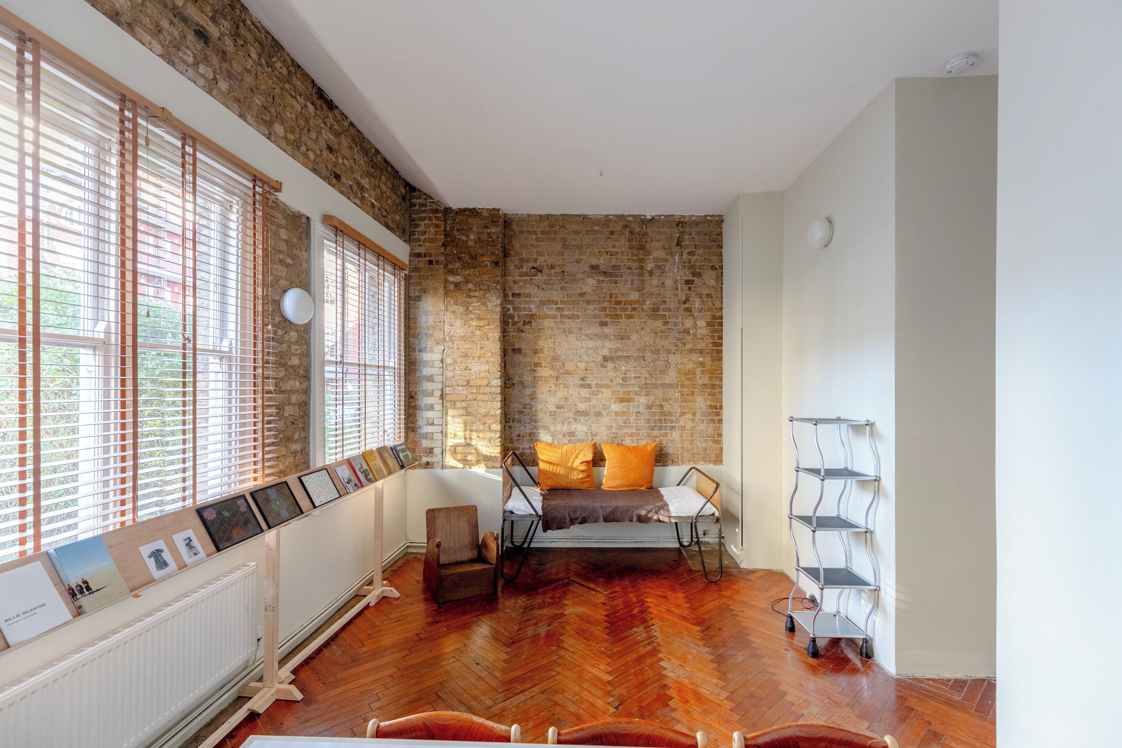 A room with a brick wall, wooden flooring, a bed with orange pillows, and a radiator.