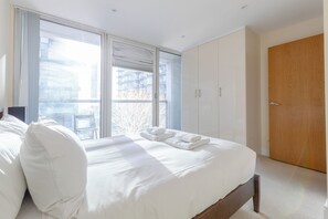 A modern bedroom with a large bed, a wooden wardrobe, and a sliding glass door leading to a balcony. - Mid Century 2 BDR Private Balcony Canary (London)