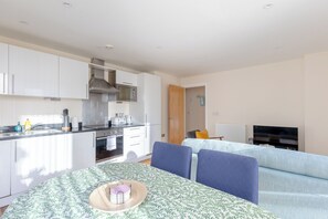 A compact living space with a kitchenette, a dining area with a table and chairs, and a seating area with a sofa. - Mid Century 2 BDR Private Balcony Canary (London)