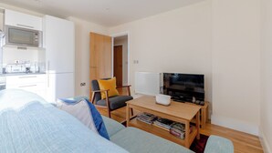 Un salon moderne comprenant un canapé, une table basse, un téléviseur et un coin cuisine avec un four à micro-ondes.