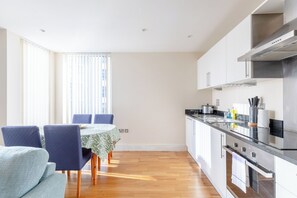 A modern kitchen with a stove, oven, and sink. There is a dining area with a table and chairs. - Mid Century 2 BDR Private Balcony Canary (London)