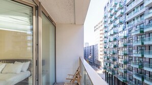 Un balcon aménagé avec un canapé et des fauteuils, donnant sur un immeuble moderne doté de nombreux balcons.