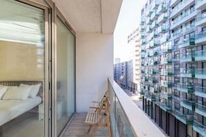 A balcony with a sofa and chairs, overlooking a modern building with multiple balconies. - Mid Century 2 BDR Private Balcony Canary (London)