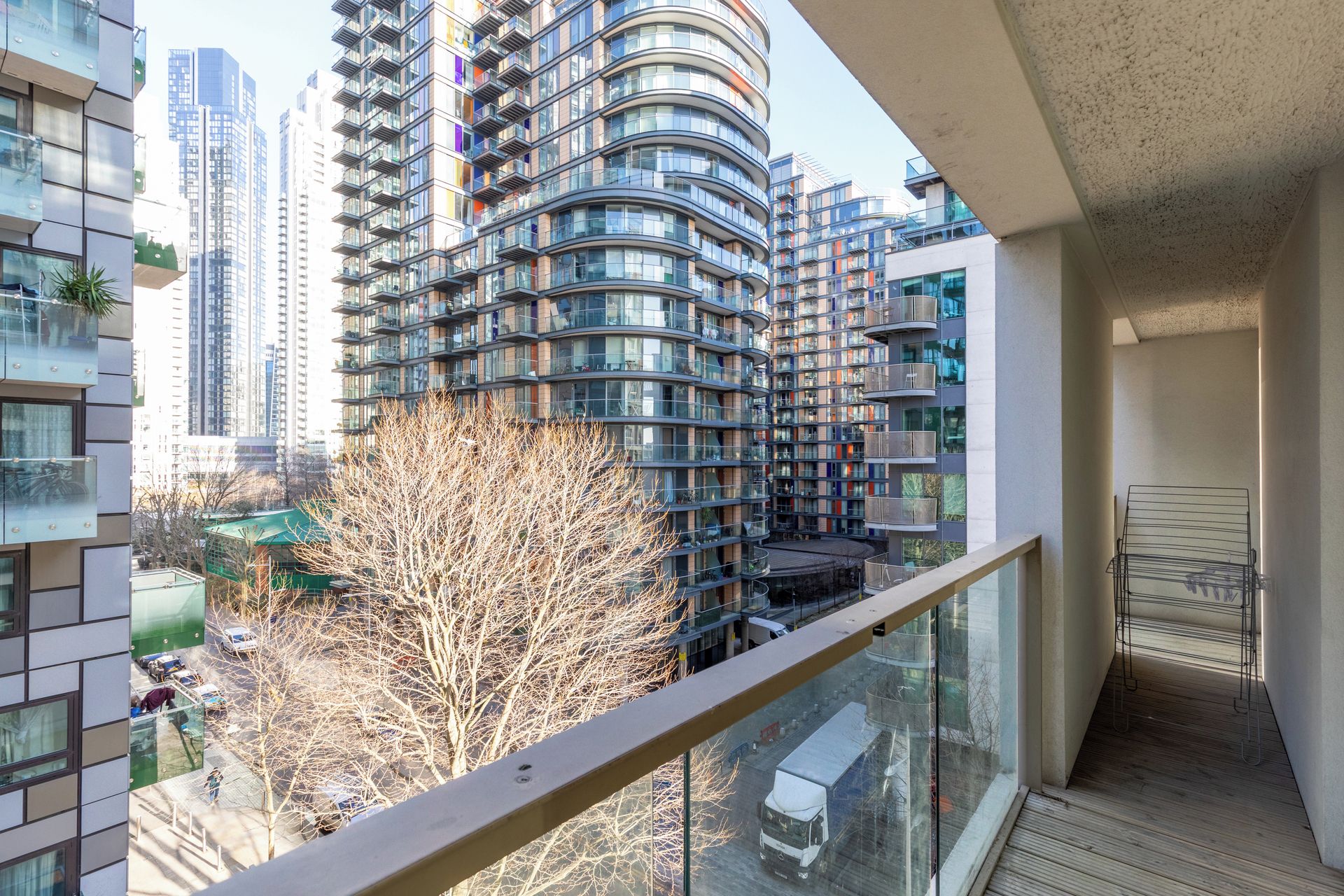 Un immeuble d’appartements moderne, doté d’une façade incurvée, de balcons et offrant une vue sur un arbre et des voitures garées.