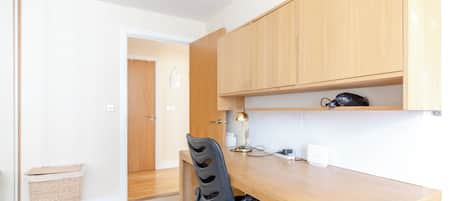 A compact kitchen with wooden cabinets, a desk, and a chair.