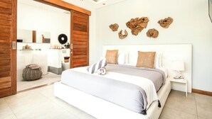 A modern bedroom with a large bed, wooden accents, a white nightstand, and a wall-mounted artwork.