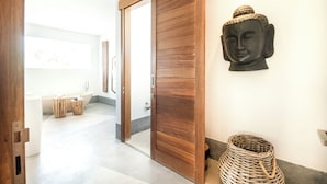 A modern bathroom with a large bathtub, wooden door, and a wall-mounted Buddha statue.