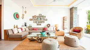 Una sala de estar moderna con un sofá seccional, otomanas, una mesa de centro de vidrio y una pared decorada con fotografías enmarcadas.