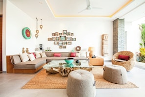 A modern living room with a sectional sofa, ottomans, a glass coffee table, and a wall decorated with framed pictures. - Chic 2BR Villas, Brawah Hub, 300m to Coastal Bliss (Canggu)