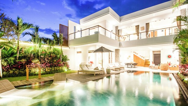 Una casa moderna de dos pisos con piscina, mobiliario exterior y un jardín cuidado.