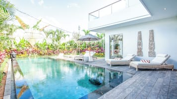 A modern pool area with lounge chairs, a glass-enclosed room, and tropical plants.