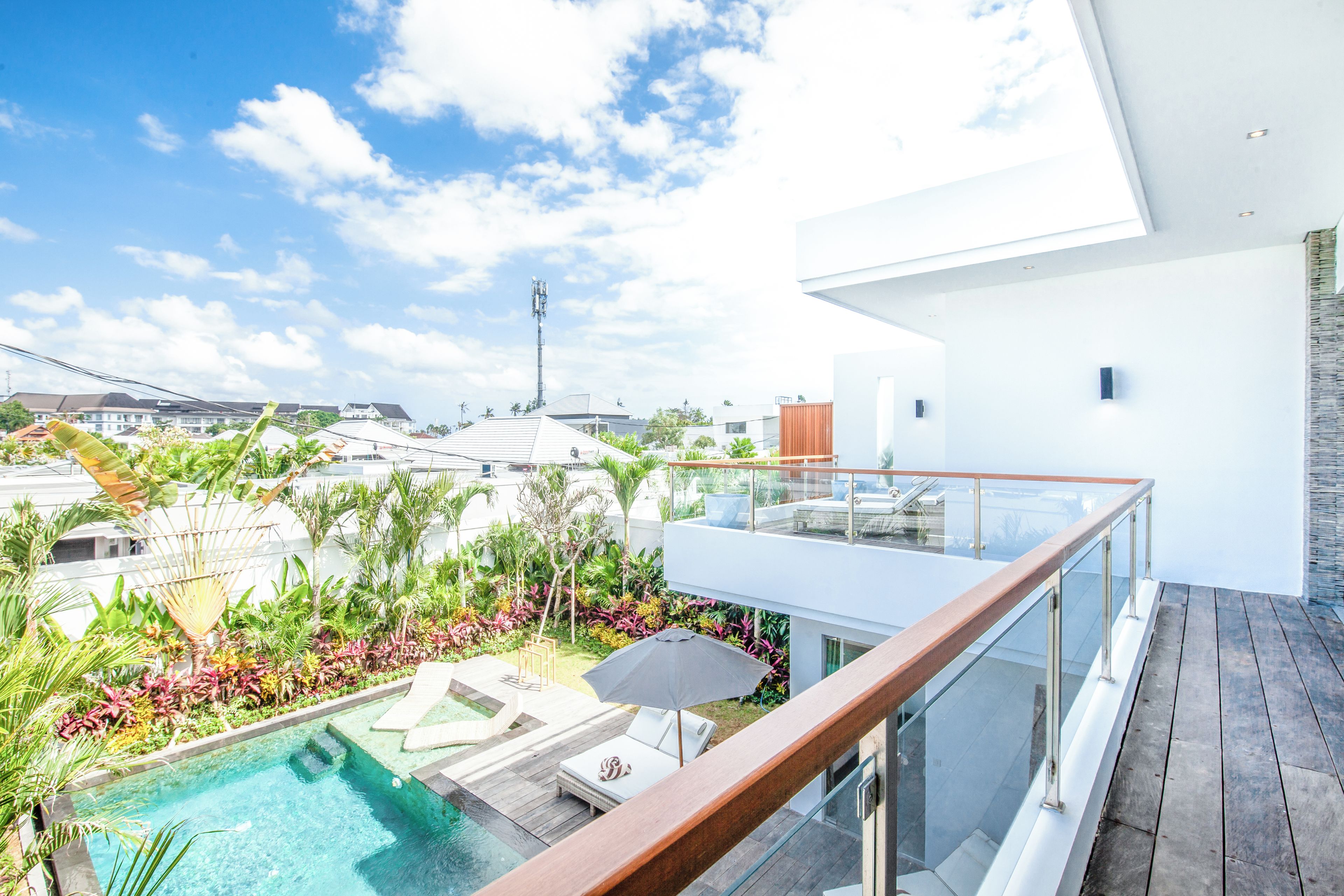 Un espace piscine extérieur moderne, doté d’une balustrade en verre, de chaises longues et d’une variété de plantes tropicales.