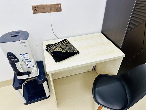 A small office space with a water dispenser, a desk with a patterned cloth, and a black office chair. - Beautiful 1-bed Studio in Dhaka (Dhaka)