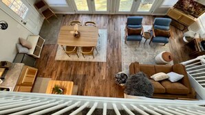 Un amplio salón con suelo de madera, una mesa de comedor, sillas azules, un sofá marrón y una escalera que lleva a un nivel superior.