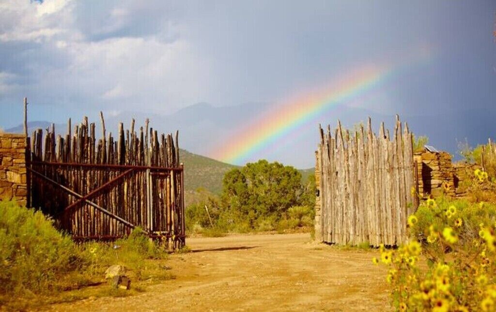 A rustic wooden gate in a natural landscape with a rainbow in the background.