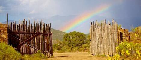 A rustic wooden gate in a natural landscape with a rainbow in the background.
