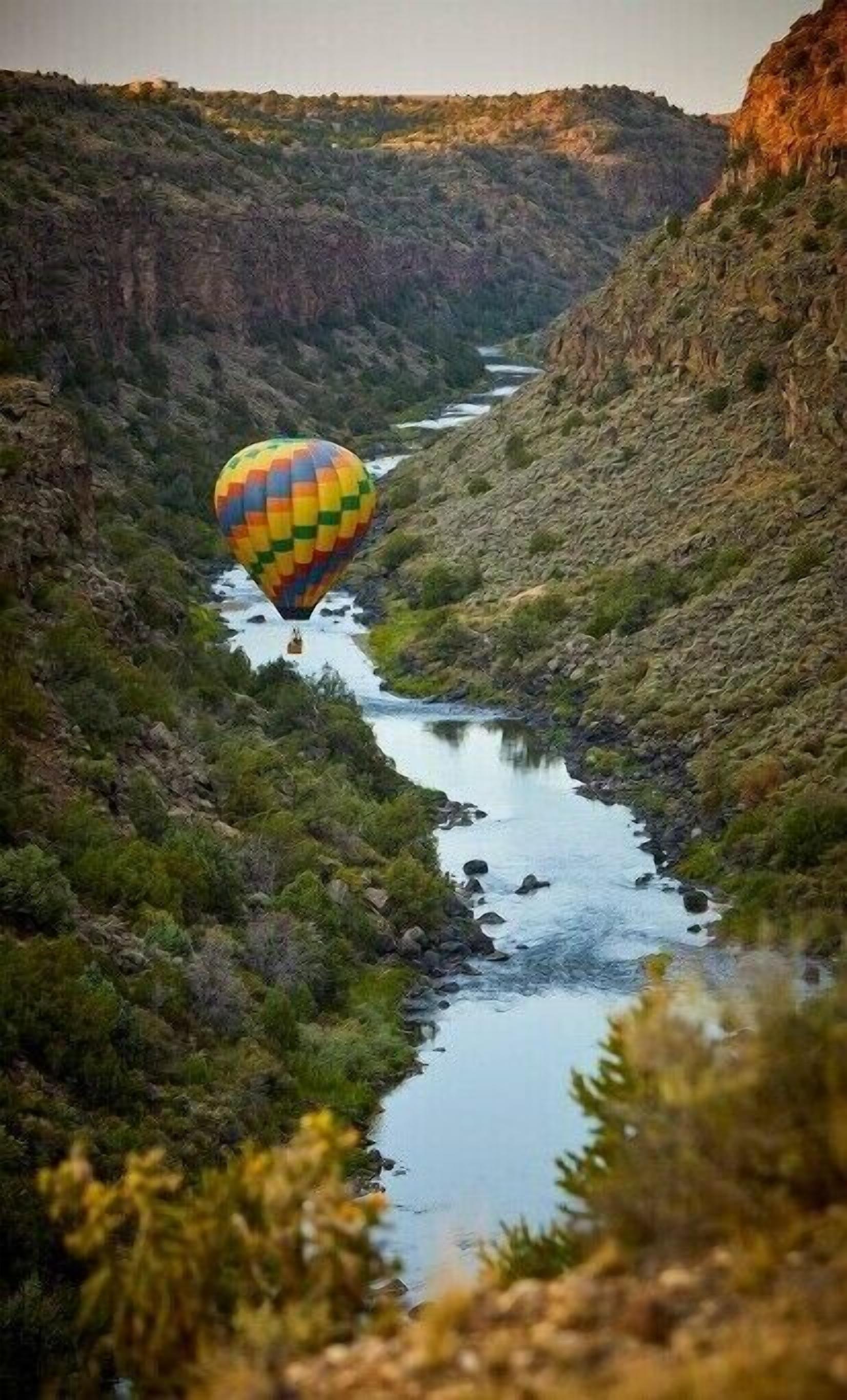 A hot air balloon over a river canyon with rocky terrain and sparse vegetation.