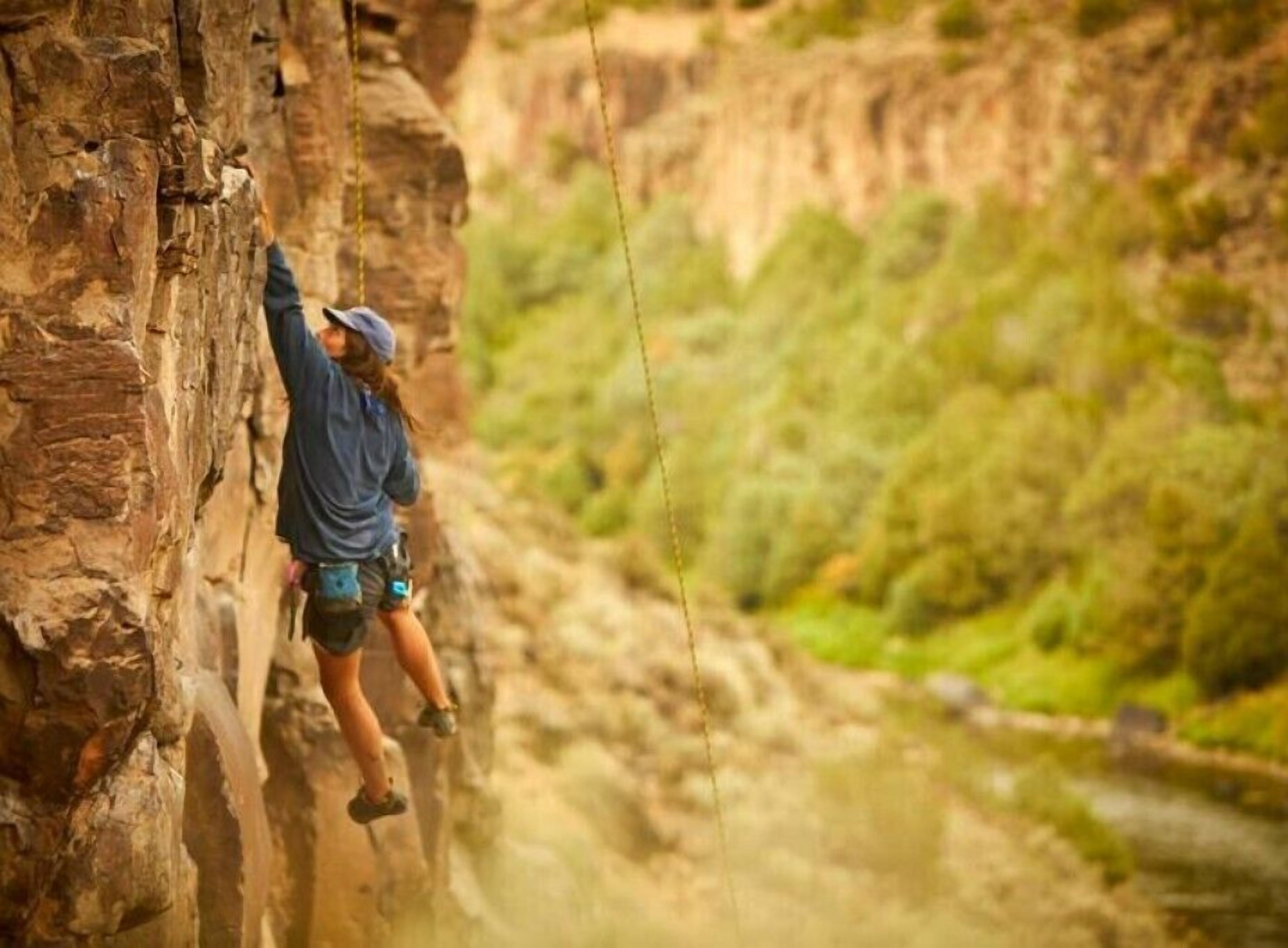 Una persona escalando una pared rocosa con un río al fondo.