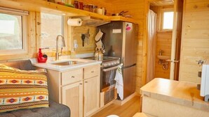 Interior d'una cabana de fusta senzilla, amb cuina americana, sofà i bany petit.