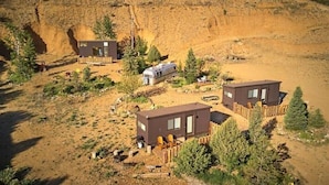 Paisatge desèrtic amb dues cabanes modernes envoltades d'arbres i un penya-segat rocós.
