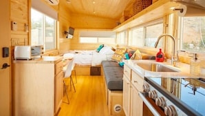Interior d'una cabana de fusta acollidora, amb petita cuina, zona de menjador i espai per dormir.