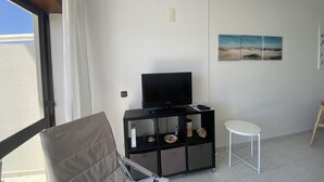 A room with a television on a black stand, a white chair, a small white table, and a beach-themed painting on the wall. - Baia - With a bay View (Alcobaça)