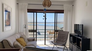 A living room with a sofa, a chair, a TV, and a balcony with a view of the sea. - Baia - With a bay View (Alcobaça)