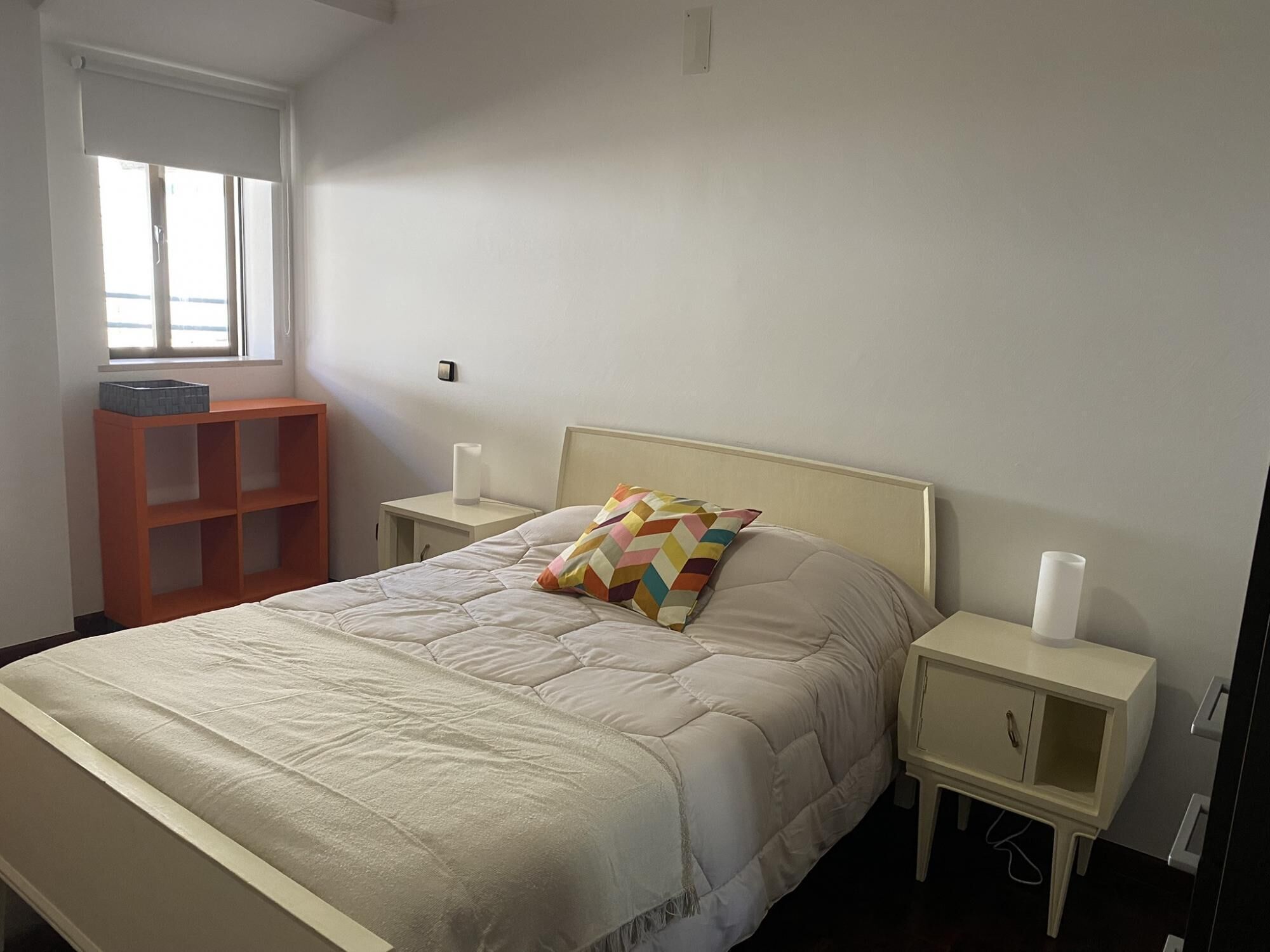 Une chambre à coucher comprenant un lit, deux tables de chevet, une commode, une fenêtre et une étagère.