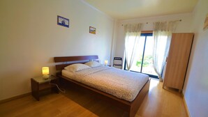 A bedroom with a wooden bed, a nightstand with a lamp, and a window with curtains. - Estrela do Mar - Com Vista Para a Piscina (Alcobaça)