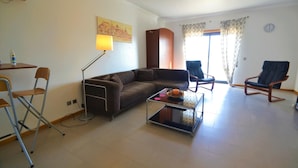 A living room with a brown sofa, a glass coffee table, a lamp, and two chairs. - Estrela do Mar - Com Vista Para a Piscina (Alcobaça)