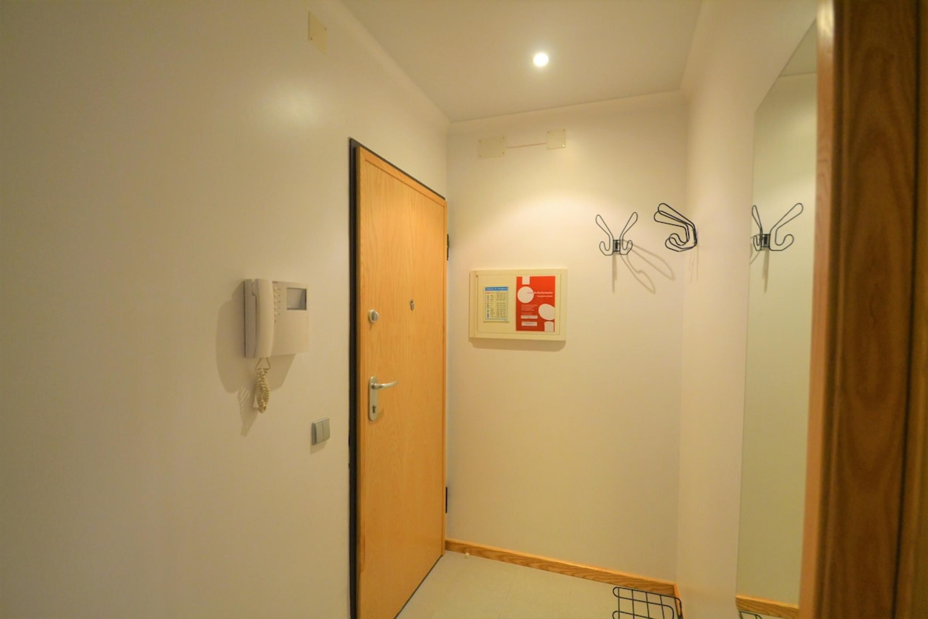 A narrow hallway with a wooden door, a wall-mounted telephone, and a framed informational poster.