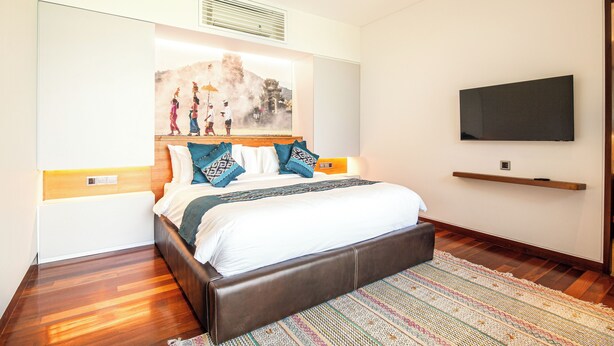 Una habitación de hotel moderna con una cama grande, un televisor de pantalla plana y una obra de arte en la pared que representa una escena tradicional.