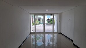 A hallway with a glass door leading outside, a tiled floor, and white walls. - OYO Life 93106 Apartement Grand Sentraland By Andi (Karawang)