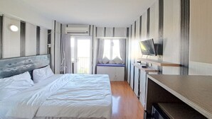 A hotel room with a bed, a TV on a stand, a window with curtains, and an air conditioning unit. - OYO Life 93106 Apartement Grand Sentraland By Andi (Karawang)