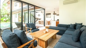 A modern living room with a large sectional sofa, a wooden coffee table, and a dining area with a kitchen in the background. - New 4BR Villa 200m to the Beach Canggu (Munggu)
