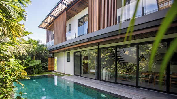 A modern house with a swimming pool, large windows, and a wooden deck. - New 4BR Villa 200m to the Beach Canggu (Munggu)