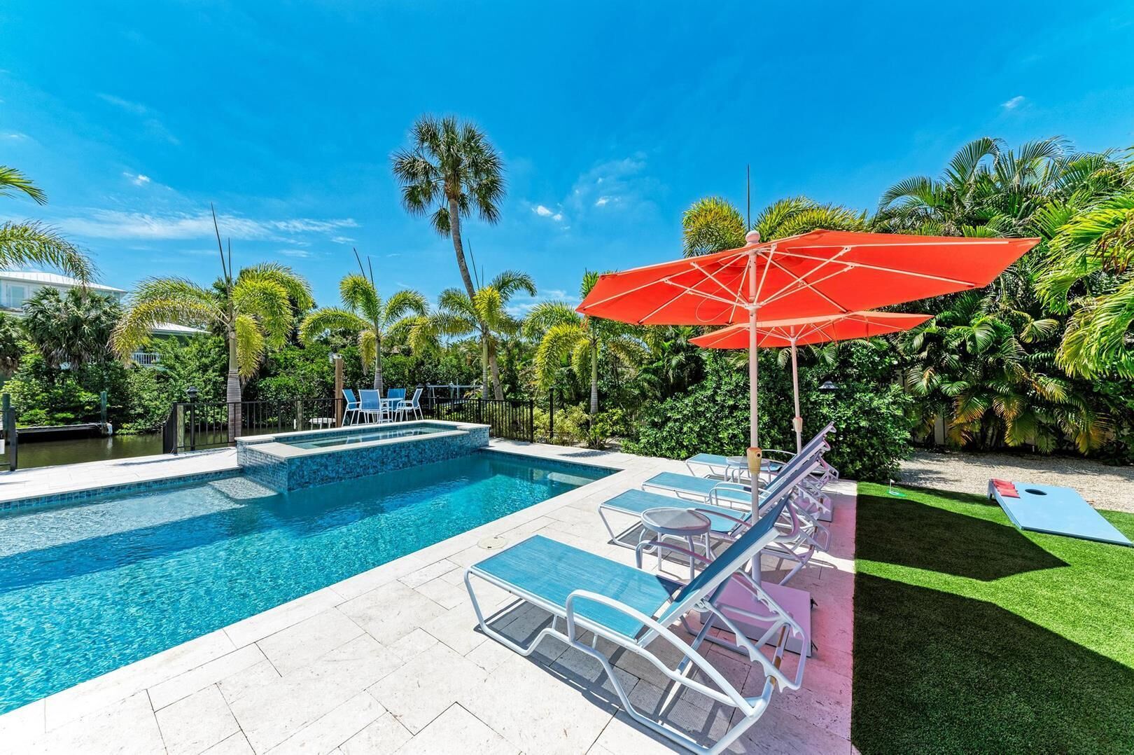 A swimming pool with lounge chairs and a red umbrella, surrounded by palm trees and greenery.
