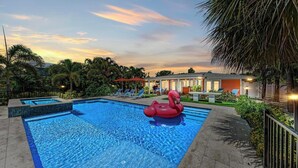 Ein Swimmingpool mit einem roten, aufblasbaren Flamingo, umgeben von Palmen und Liegestühlen.