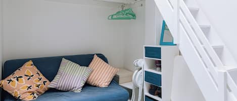 Une pièce avec un canapé bleu, un escalier blanc et un porte-manteau vert accroché au mur.