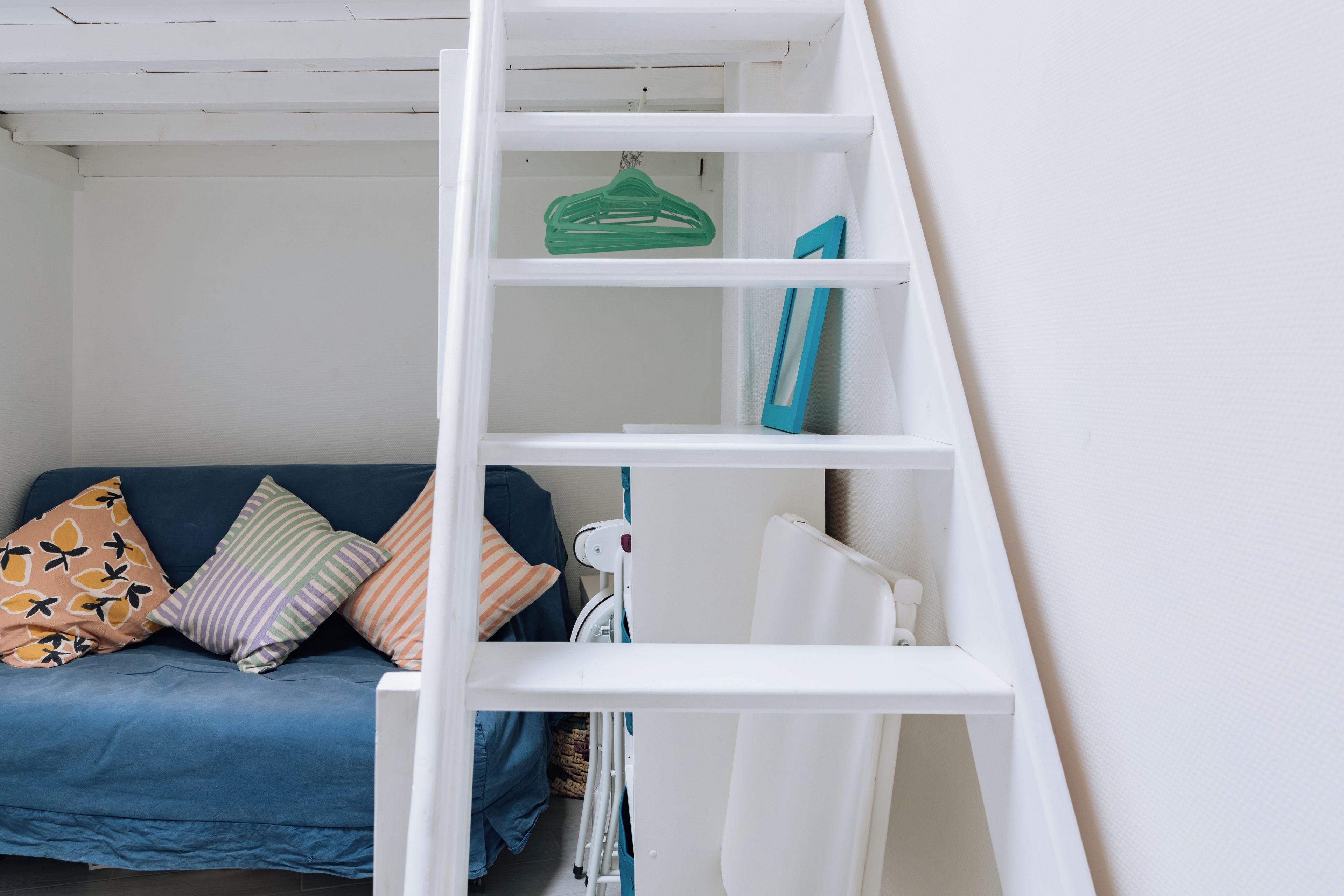 A white ladder leaning against a wall with a blue sofa and pillows in the background.