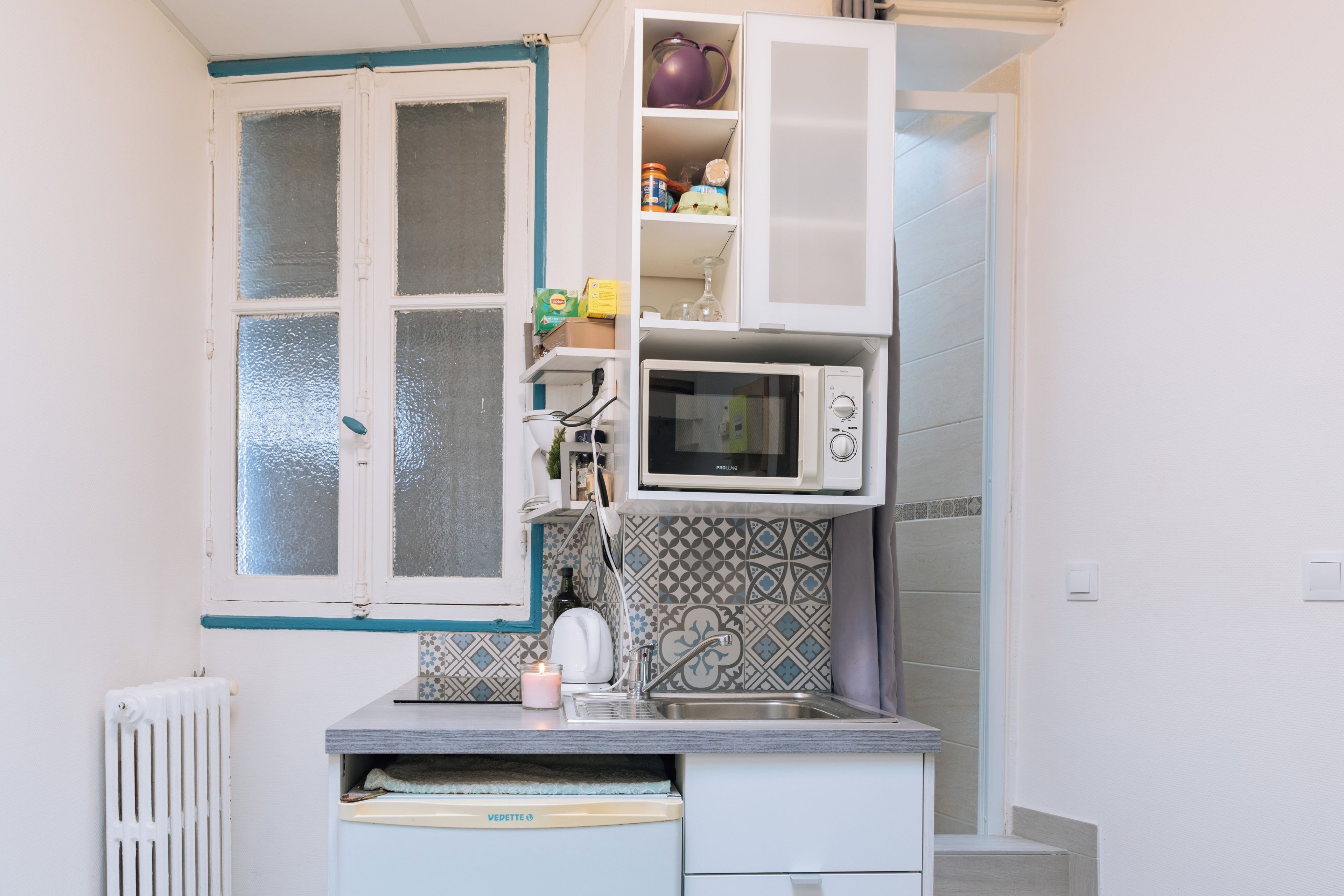 A compact kitchen with a window, a microwave, and a small refrigerator.