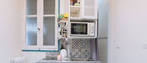 A compact kitchen with a window, a microwave, and a small refrigerator.