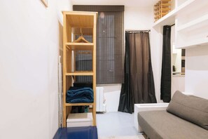 A compact living space with a wardrobe, a sofa, a radiator, and a window with curtains.